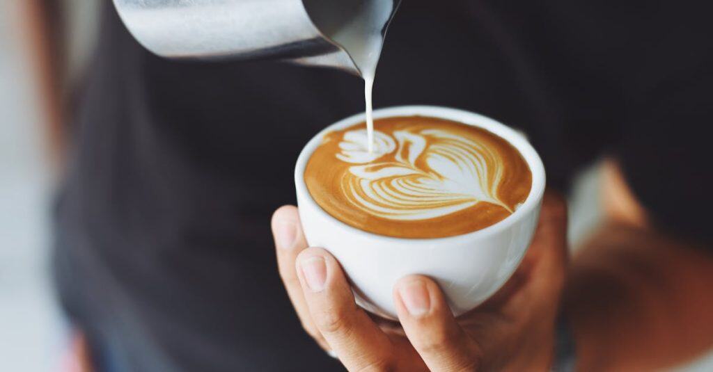 Close-up of a barista pouring milk to create latte art in a coffee cup.