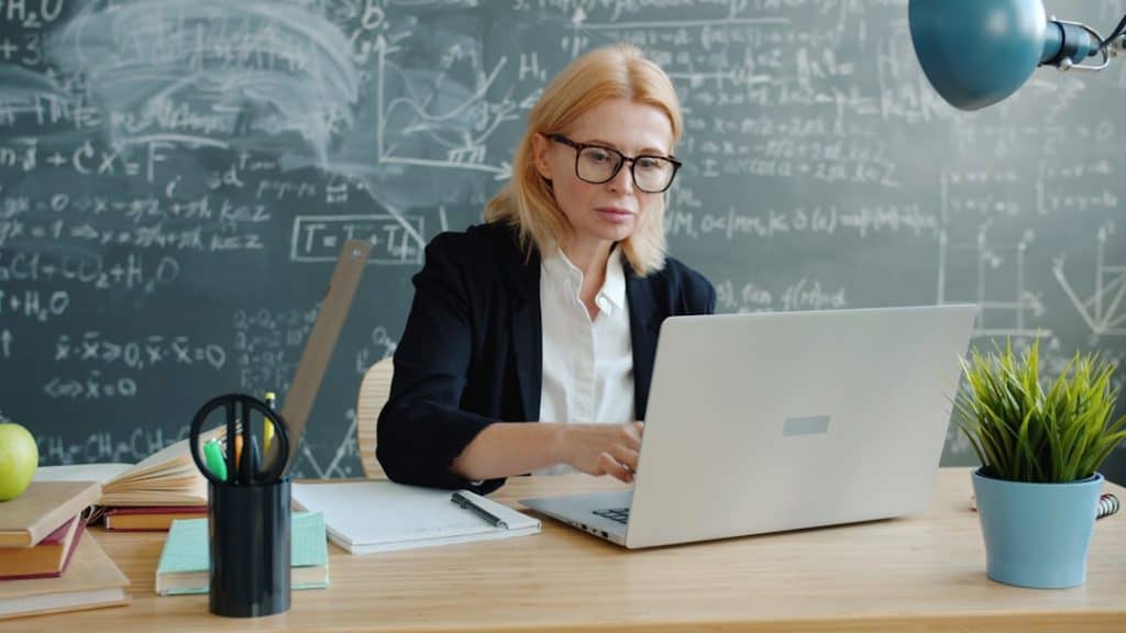 Photo by Vitaly Gariev Woman working on a laptop in front of a chalkboard.