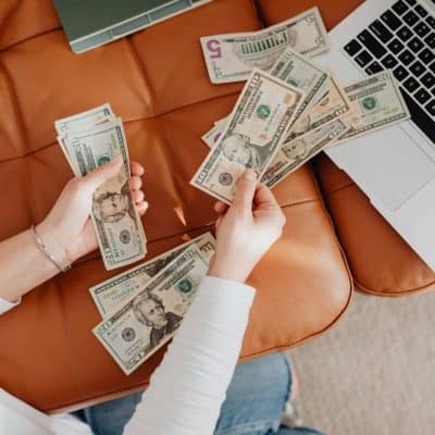 hands holding cash by a computer on a couch