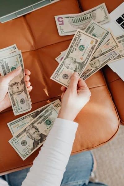 hands holding cash by a computer on a couch