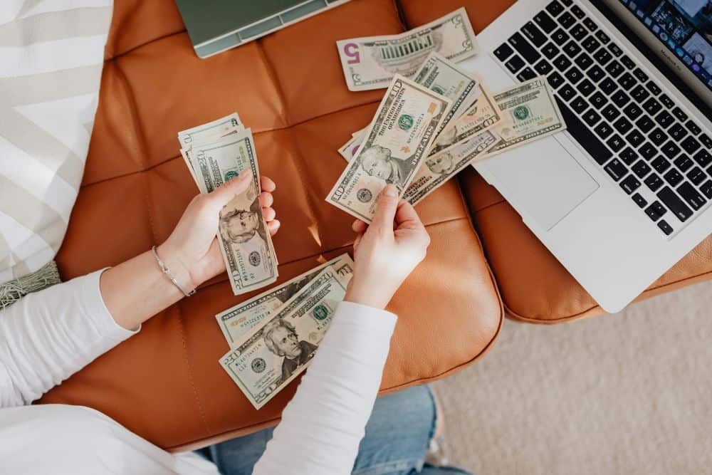 hands holding cash by a computer on a couch