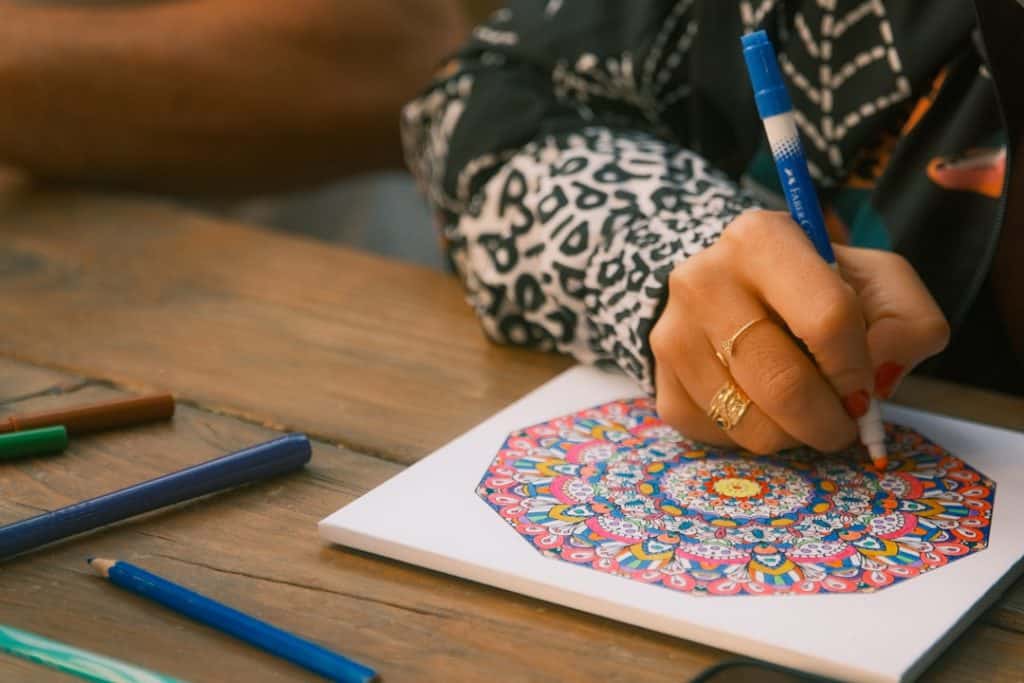Photo by Christian Harb Person coloring a mandala with markers on paper