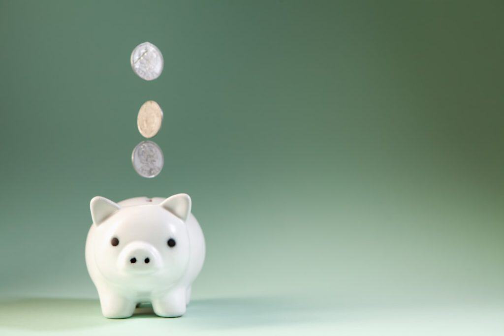 Photo by Sasun Bughdaryan Coins falling into a white piggy bank.